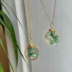 Two gold necklaces with green stone pendants on a neutral background