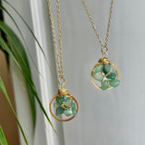 Two gold necklaces with green stone pendants on a neutral background