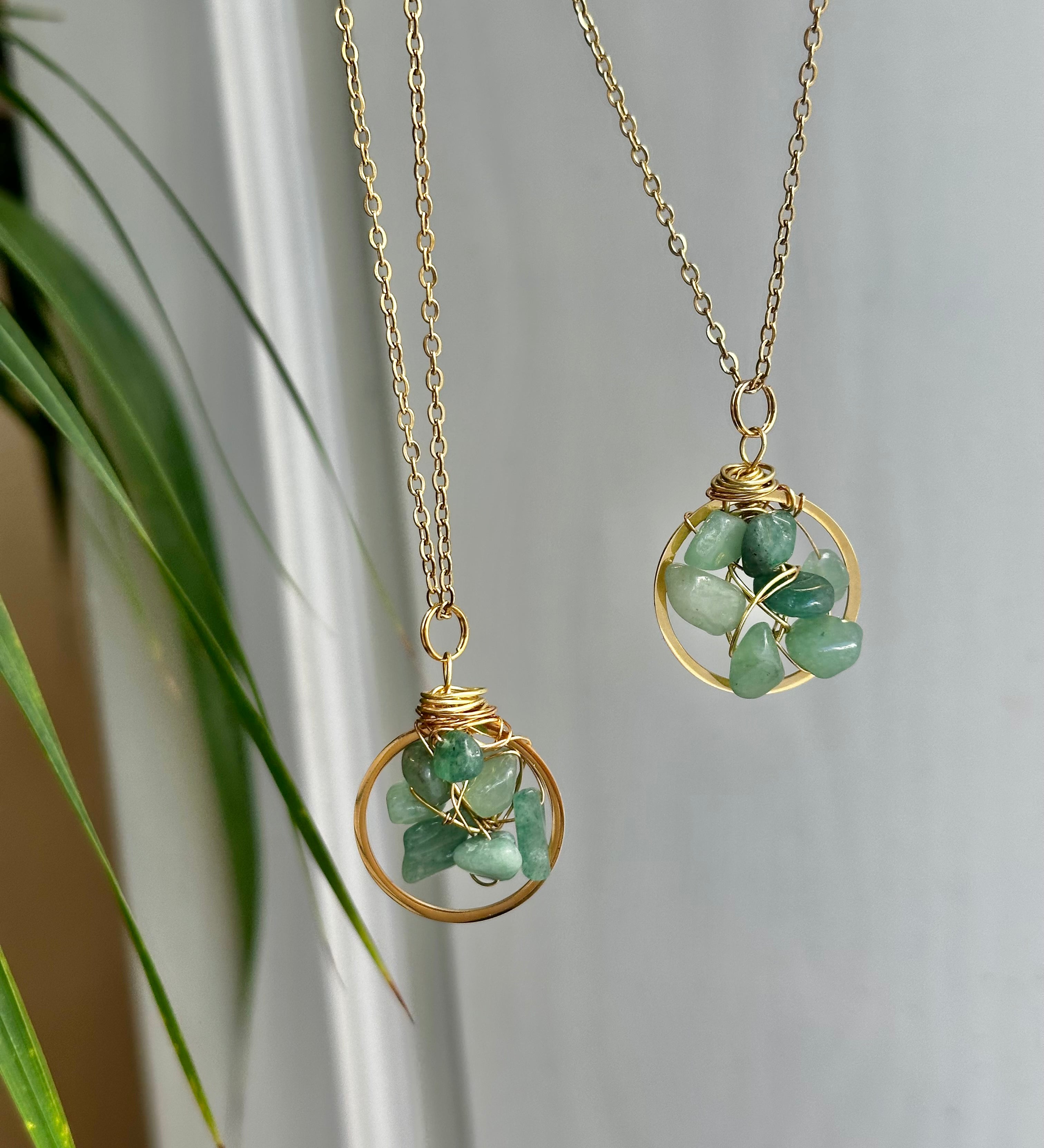 Two gold necklaces with green stone pendants on a neutral background