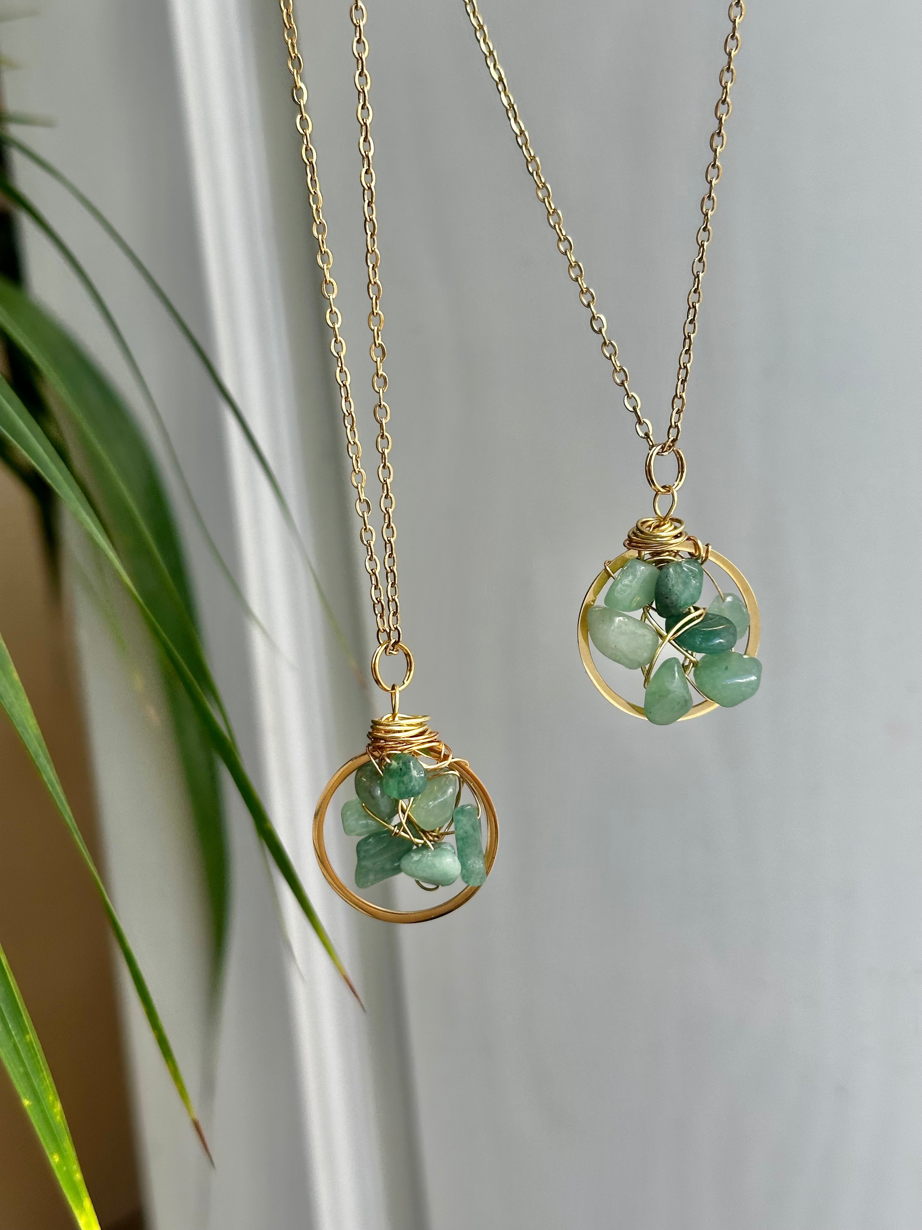 Two gold necklaces with green stone pendants on a neutral background