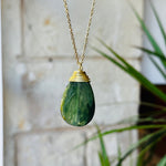 Green teardrop pendant necklace with gold chain against a blurred background