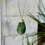 Green teardrop pendant necklace with gold chain against a blurred background