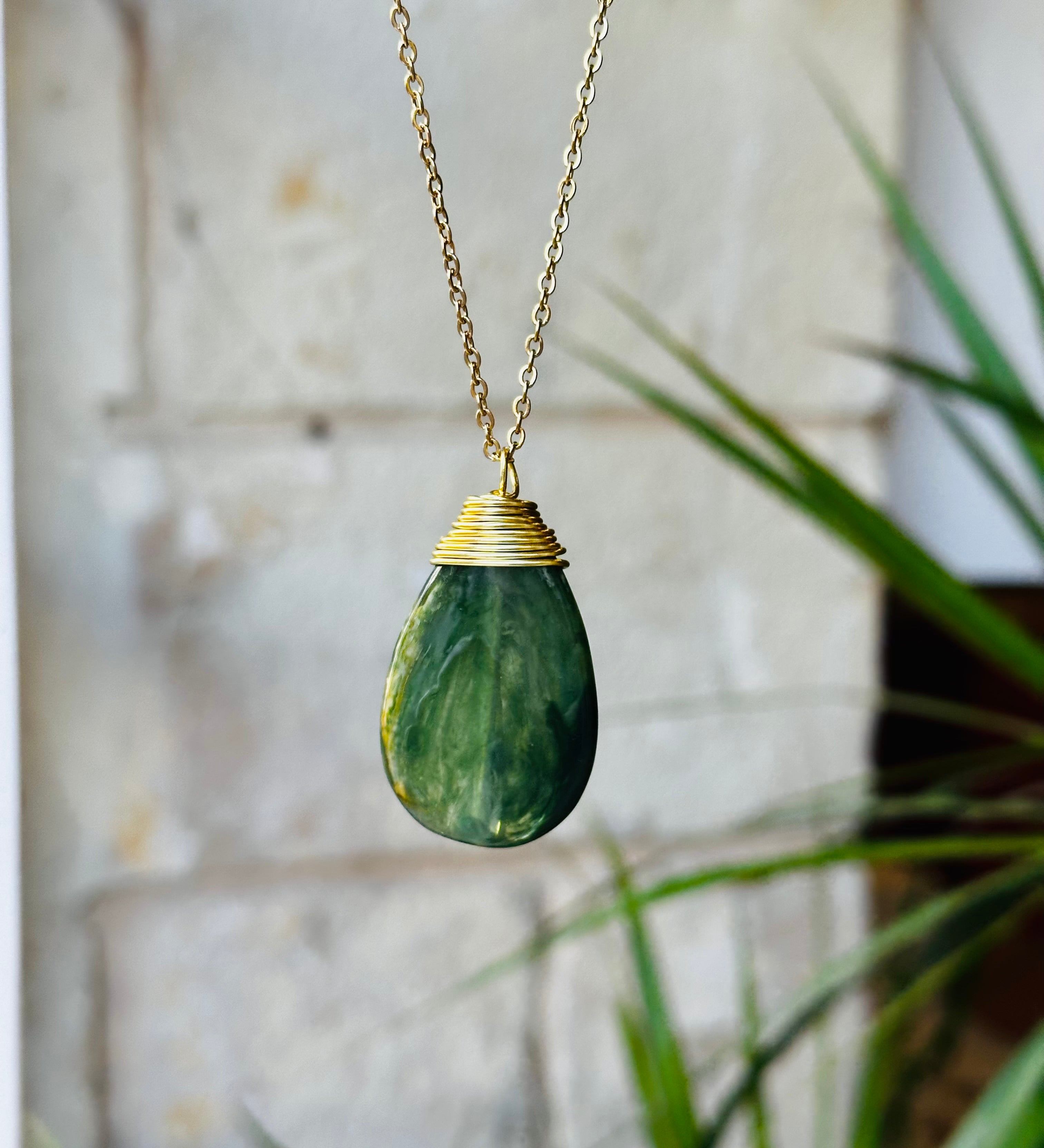 Green teardrop pendant necklace with gold chain against a blurred background
