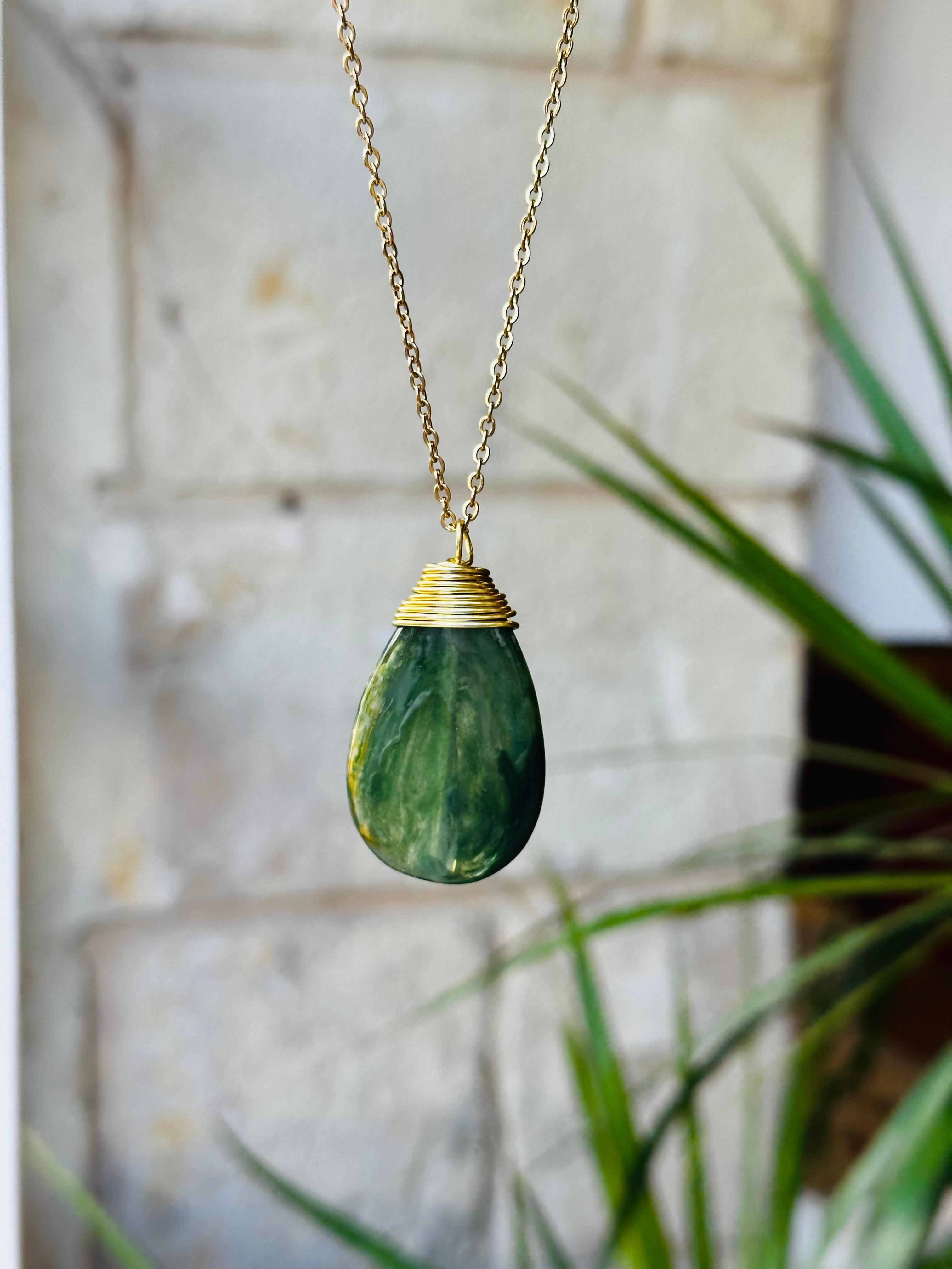 Green teardrop pendant necklace with gold chain against a blurred background